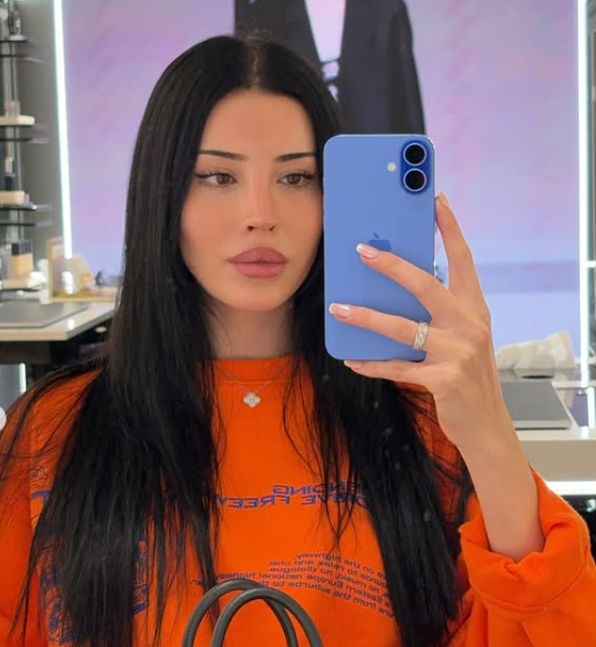 Confident woman taking a mirror selfie in an orange top, symbolizing mastering her fears and building the life she deserves.