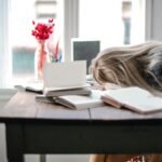 Woman exhausted at desk surrounded by open books, symbolizing mental burnout from constantly overthinking and wondering how to stop over explaining myself.